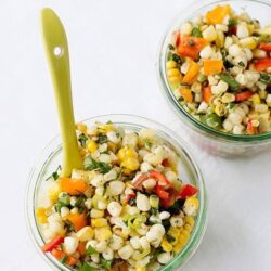 Bright corn and vegetable salad in glass bowls with a lime green serving spoon, fresh and colorful, perfect for healthy eating.