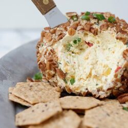 Cream cheese and chopped nuts stuffed cheese ball with crackers on a plate.
