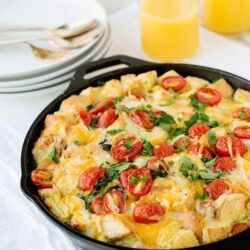 Creamy breakfast casserole with cherry tomatoes and fresh herbs in a skillet.