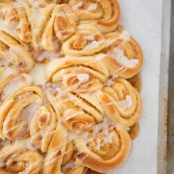Cream cheese cinnamon rolls drizzled with icing on baking sheet.