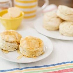 Fluffy homemade scones drizzled with honey on a white plate for breakfast or tea.