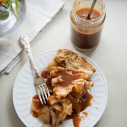 Sweet apple pie with caramel sauce and a glass of iced coffee on a white plate.