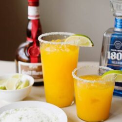 Refreshing margarita cocktails garnished with lime wedges, with salted rims, served on a white table.