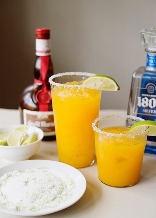 Refreshing frozen margarita with salted rims, lime wedge, and homemade margarita mix on table.