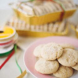 Soft sugar cookies on a pink plate with holiday ribbon and baking supplies in the background.