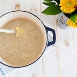 Creamy mushroom soup in a blue pot on a white wooden table with a butter knife and fresh flowers nearby.