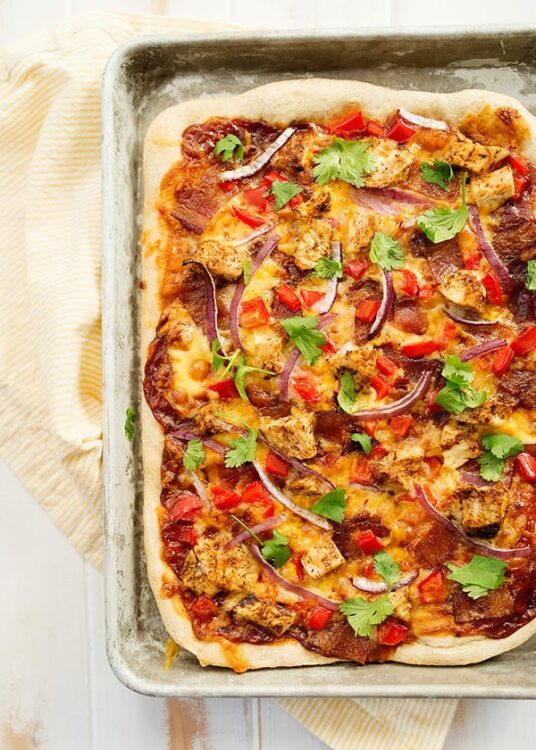 Homemade pizza with grilled chicken, peppers, red onions, and fresh cilantro on a baking sheet.