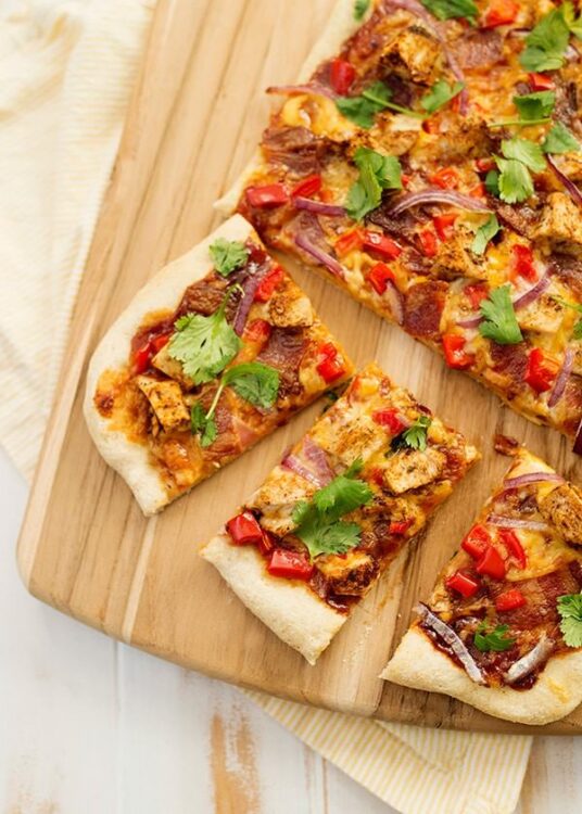 Crispy chicken pizza with red peppers and cilantro on a wooden cutting board.