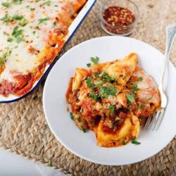 Creamy baked ziti with melted cheese and herbs served on a white plate.