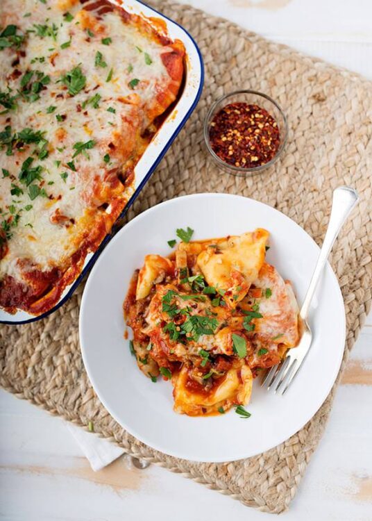 Creamy baked ziti with melted cheese and fresh herbs on a white plate.