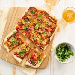 Golden baked Mexican pizza with fresh cilantro on a wooden cutting board, served with beer and a side of greens.