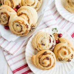 Flaky cinnamon rolls with cranberries on white plates, baked to golden perfection.