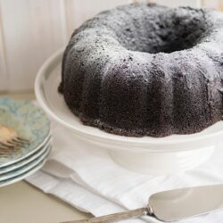 Rich chocolate Bundt cake dusted with powdered sugar on a white cake stand.