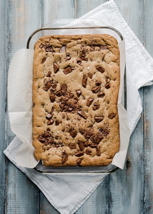 Chocolate chip cookie bar baked in a glass dish on a rustic wooden surface.