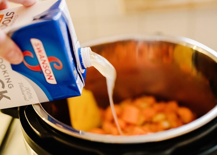 Cream being poured into a slow cooker with vegetables for a hearty stew or chili.