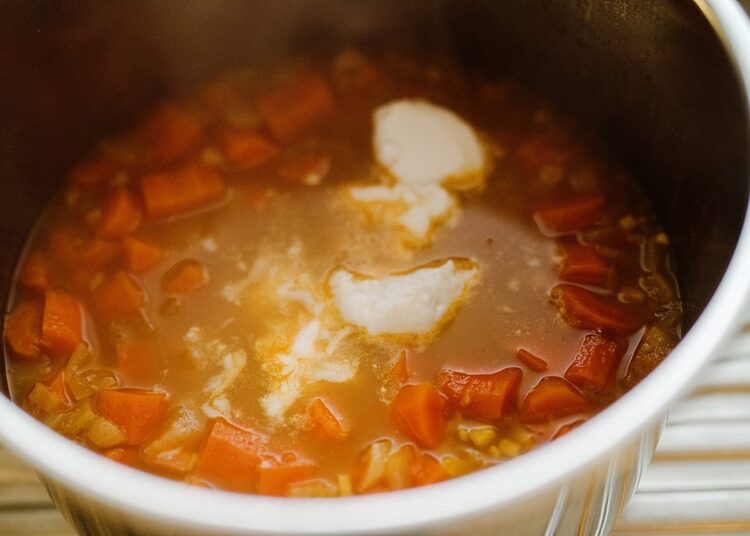 Creamy carrot soup with melted butter in a pot, ready to serve, flavorful and warming.