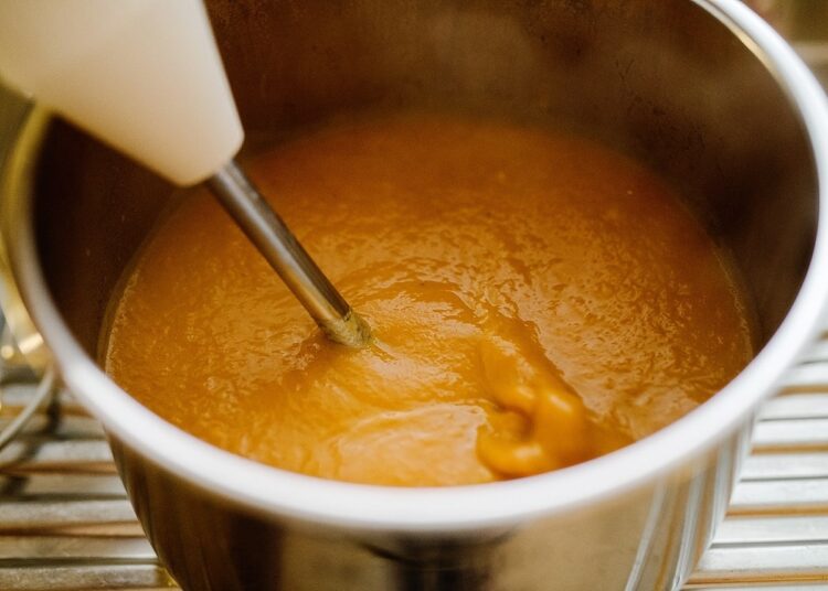 Creamy caramel sauce being stirred in a stainless steel saucepan for baking or dessert recipes.