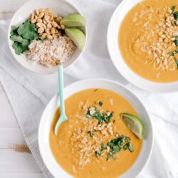 Creamy butternut squash soup garnished with herbs and chopped nuts, served with lime wedges.
