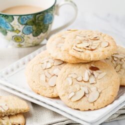 Buttery almond cookies with sliced almonds on top, served with a cup of tea or coffee on a white tray.