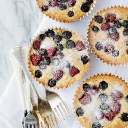 Fresh berry muffins with powdered sugar on a marble surface, baked to golden perfection.