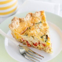 Savory vegetable quiche with cheese on a white plate.