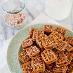 Colorful decorated caramel apple cookies on a turquoise plate with sprinkles and milk in the background, perfect for sweet bakery treats.