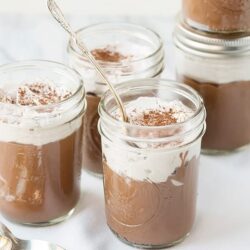 Creamy chocolate pudding in glass jars with whipped topping and cocoa powder, perfect for dessert.