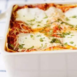 Golden baked lasagna with melted cheese and fresh herbs in a white baking dish.