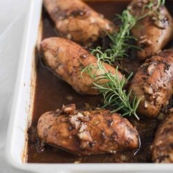 Succulent baked chicken thighs with rich gravy and fresh herbs on a white baking dish. Perfect comfort food for dinner recipes.