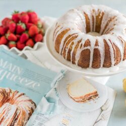Moist lemon bundt cake with white glaze and fresh strawberries on a cake stand, perfect for dessert or brunch.