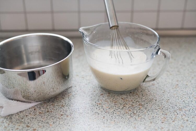 Cream batter in a glass mixing bowl with a whisk, on a kitchen countertop.