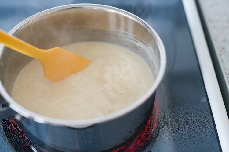 Cream being heated on stovetop with a silicone spatula, ideal for baking recipes.