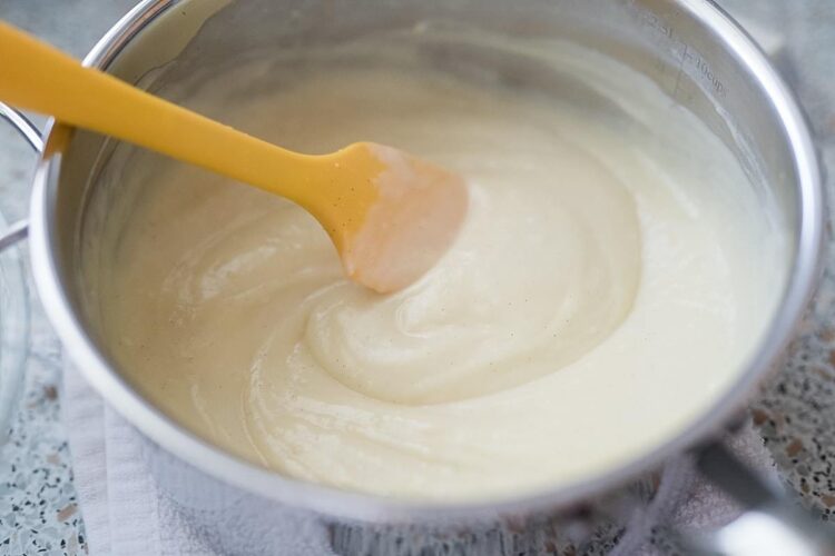 Creamy custard mixture being stirred in a stainless steel bowl with a yellow spatula, ready for baking.
