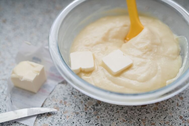 Cream cheese mixture in a glass bowl with butter cubes on counter.