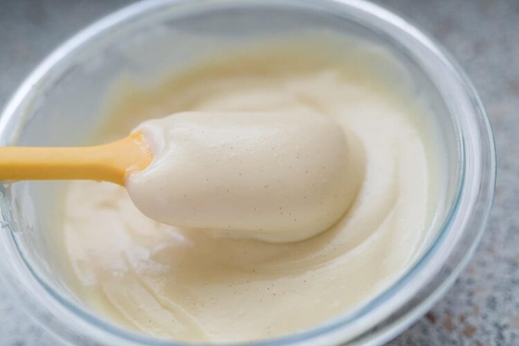 Creamy vanilla frosting in a glass bowl with a spatula for baking and decorating cakes.