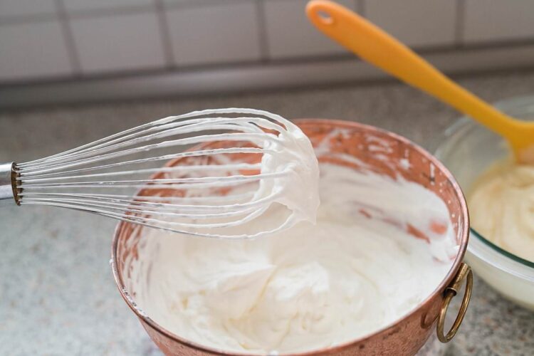 Fluffy whipped cream being mixed in a copper mixing bowl for baking recipes.
