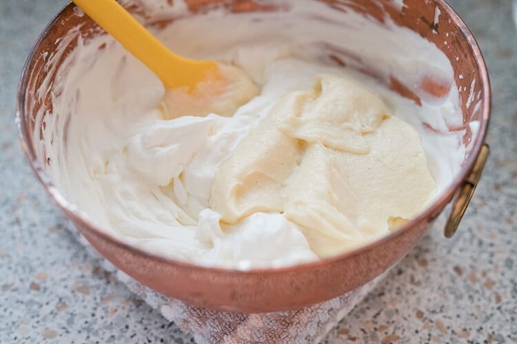 Cream cheese frosting in a copper bowl with a yellow spatula.