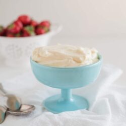 Creamy vanilla pudding in a blue dessert cup with a bowl of fresh strawberries in the background.