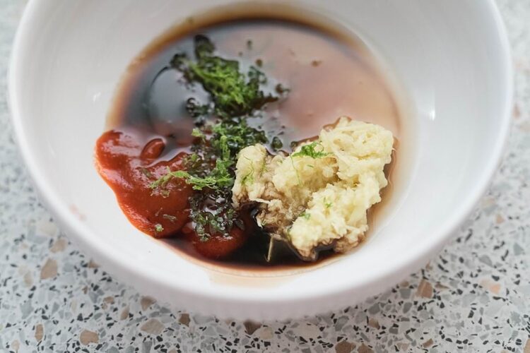Creamy mashed potatoes with gravy, herbs, and tomato sauce in a white bowl.
