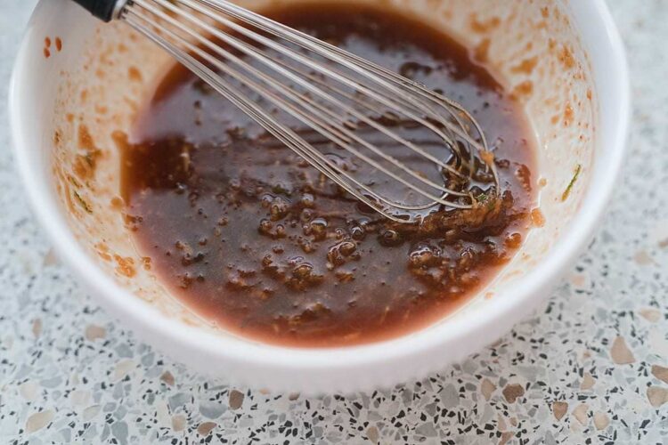 Rich chocolate cake batter being mixed in a white bowl with a metal whisk, ready for baking.