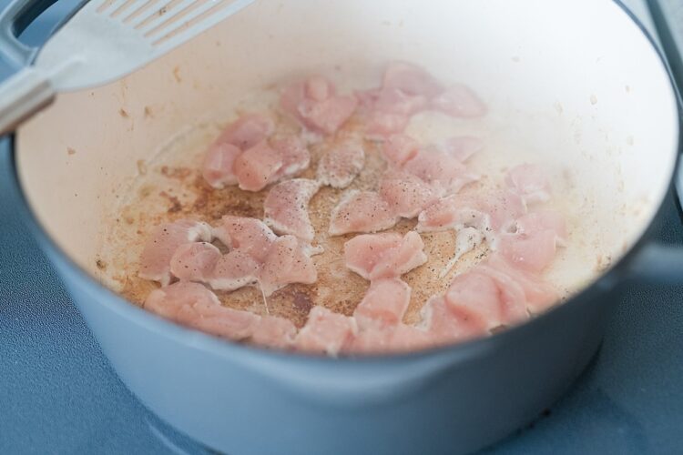 Raw chicken pieces cooking in a skillet on the stove.