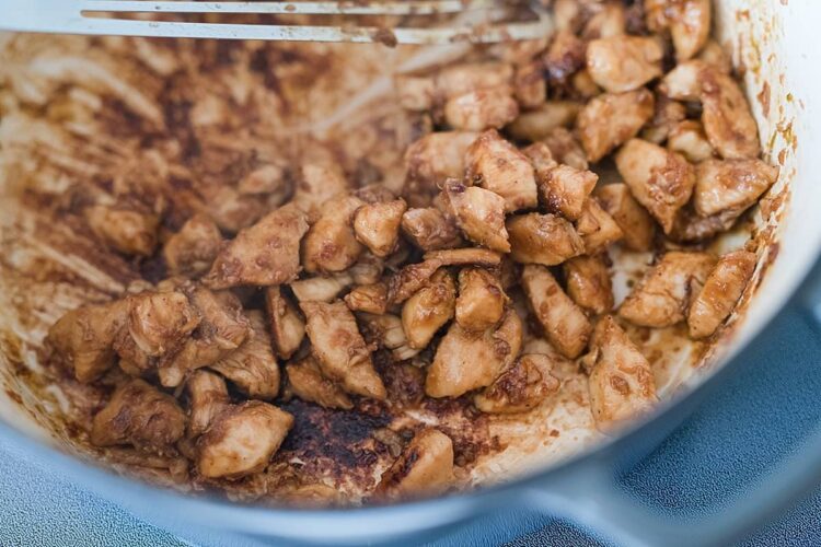 Juicy cooked chicken pieces in a white cast iron skillet.