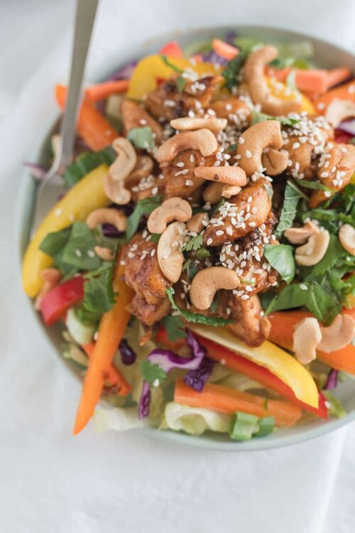 Savory Asian chicken salad with cashews, fresh vegetables, and sesame seeds in a white bowl.