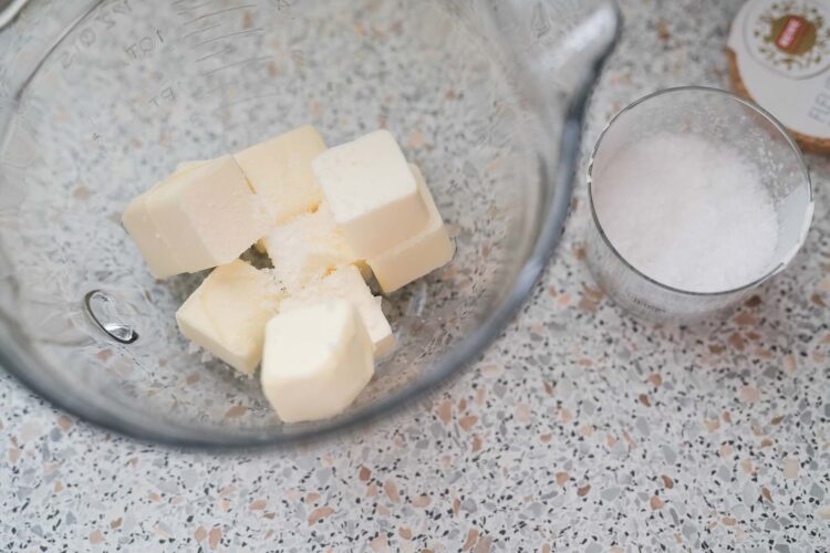 Butter cubes in glass mixing bowl with sugar and baking ingredients.