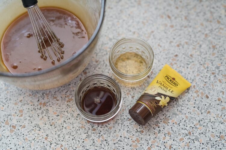 Creamy chocolate and vanilla pudding mixture with vanilla paste and extracts on a speckled countertop.