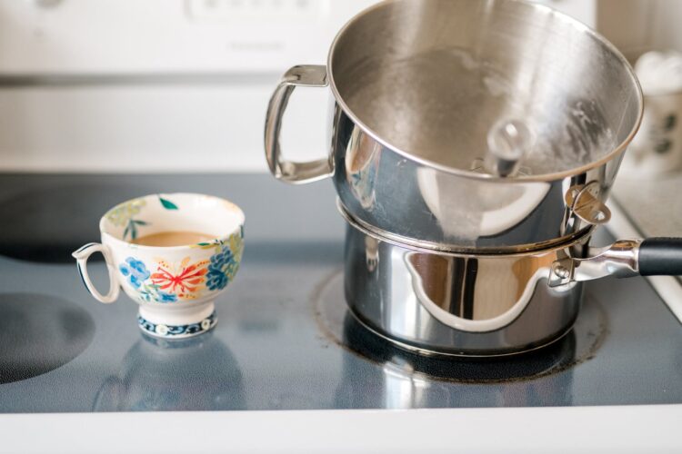 Stainless steel double boiler on stove with tea cup filled with tea and floral design.