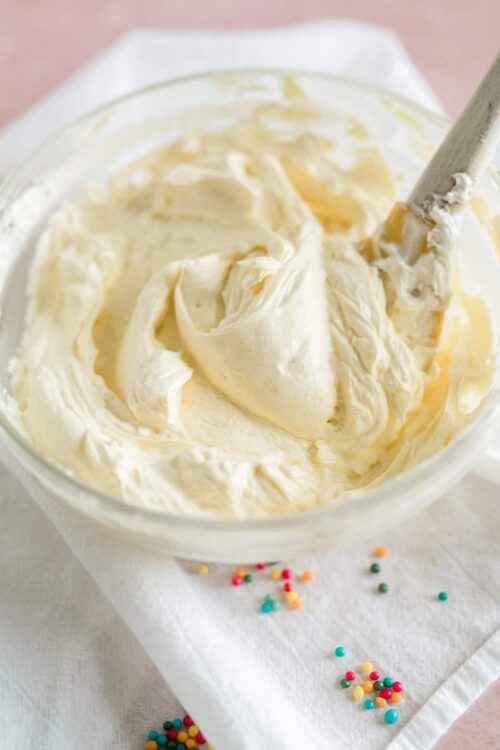Cream cheese frosting in a glass bowl with a spatula, perfect for cake decorating or baking.