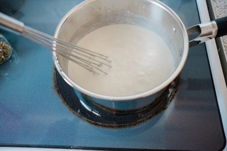 Creamy sauce simmering in a saucepan on stovetop, with a whisk stirring the mixture.