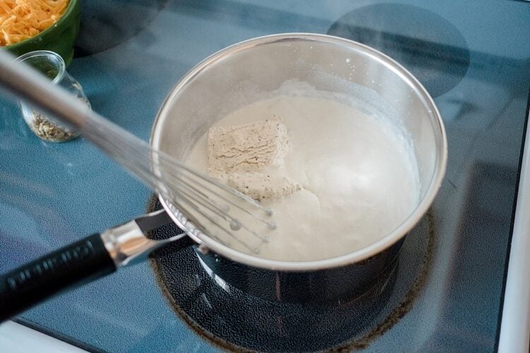 Cream cheese melting in a saucepan for a cooking recipe, whisk in progress.