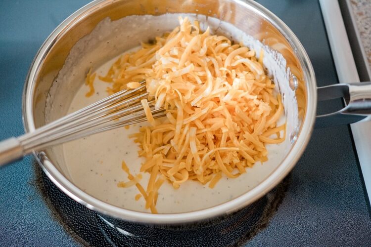 Shredded cheddar cheese in a creamy cheese sauce for baked mac and cheese.